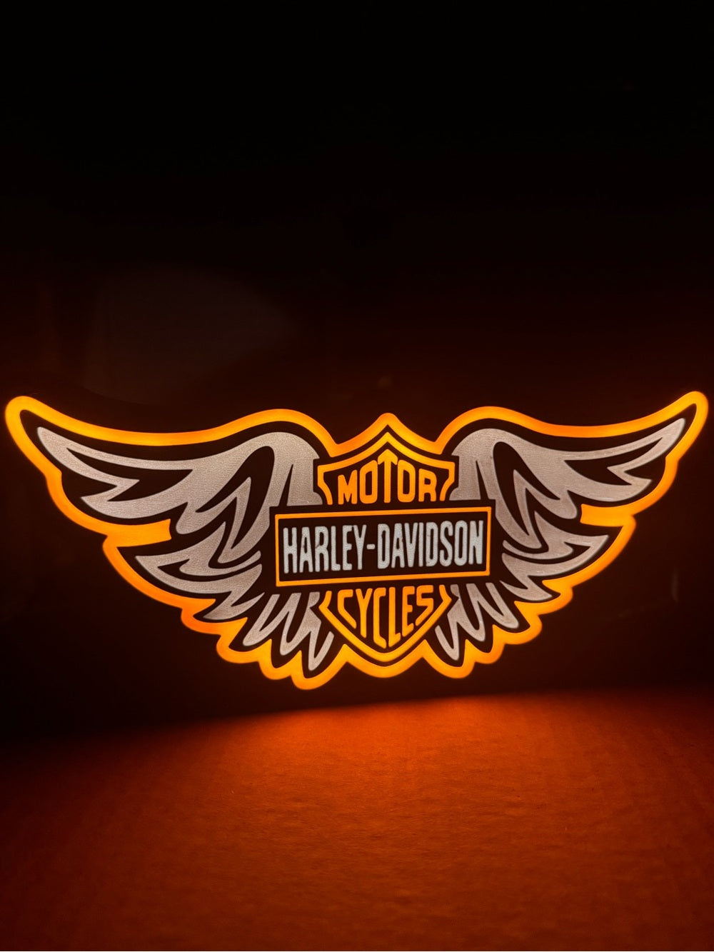 Winged motorcycle emblem light sign with orange backlight and white and black detail