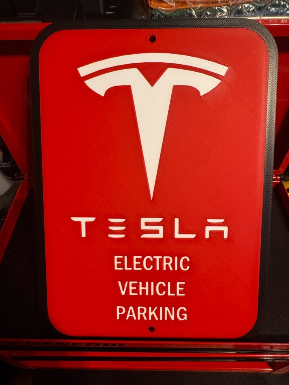 White letters, logo and outline, red background, Tesla EV parking sign in a red tool chest