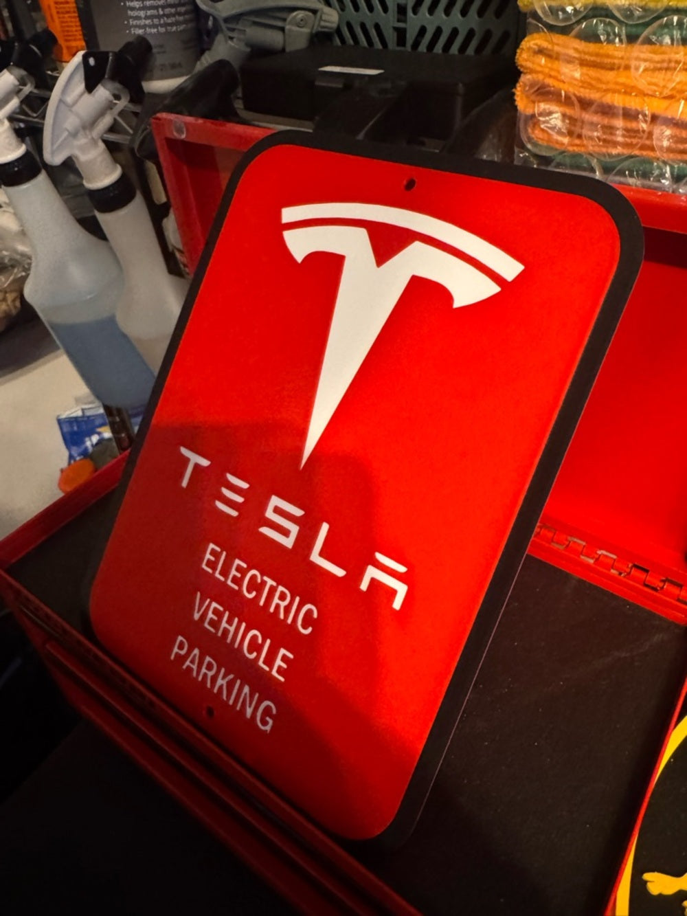 White letters, logo and outline, red background, Tesla EV parking sign in a red tool chest, angled view