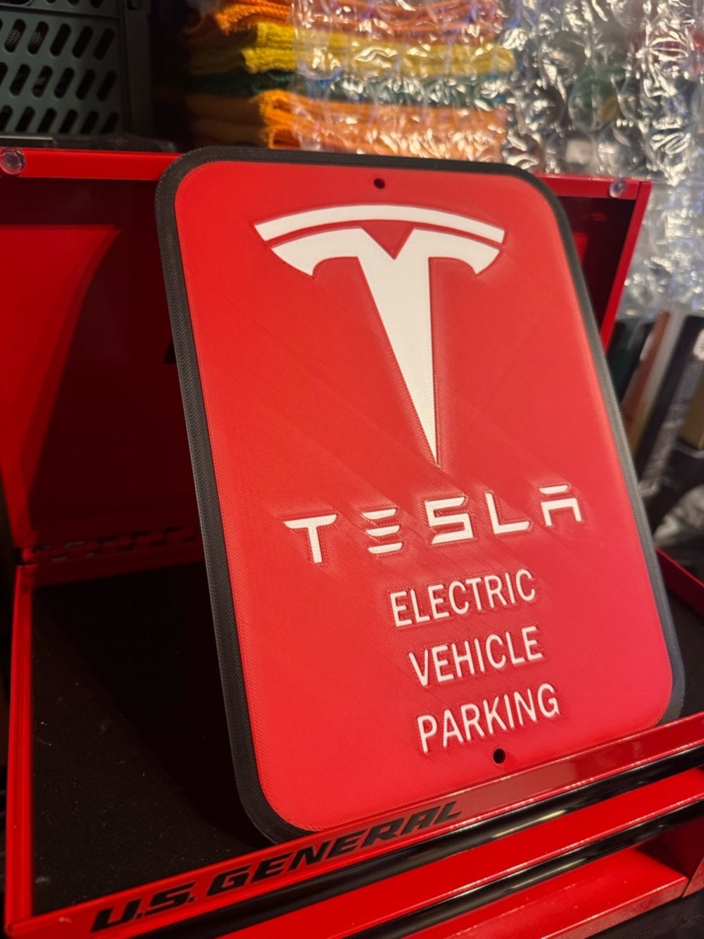 White letters, logo and outline, red background, Tesla EV parking sign in a red tool chest, side view