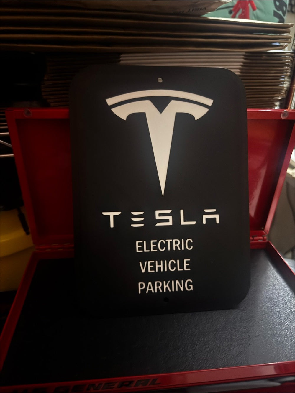 White letters, logo and outline, black background, Tesla EV parking sign in a red tool chest
