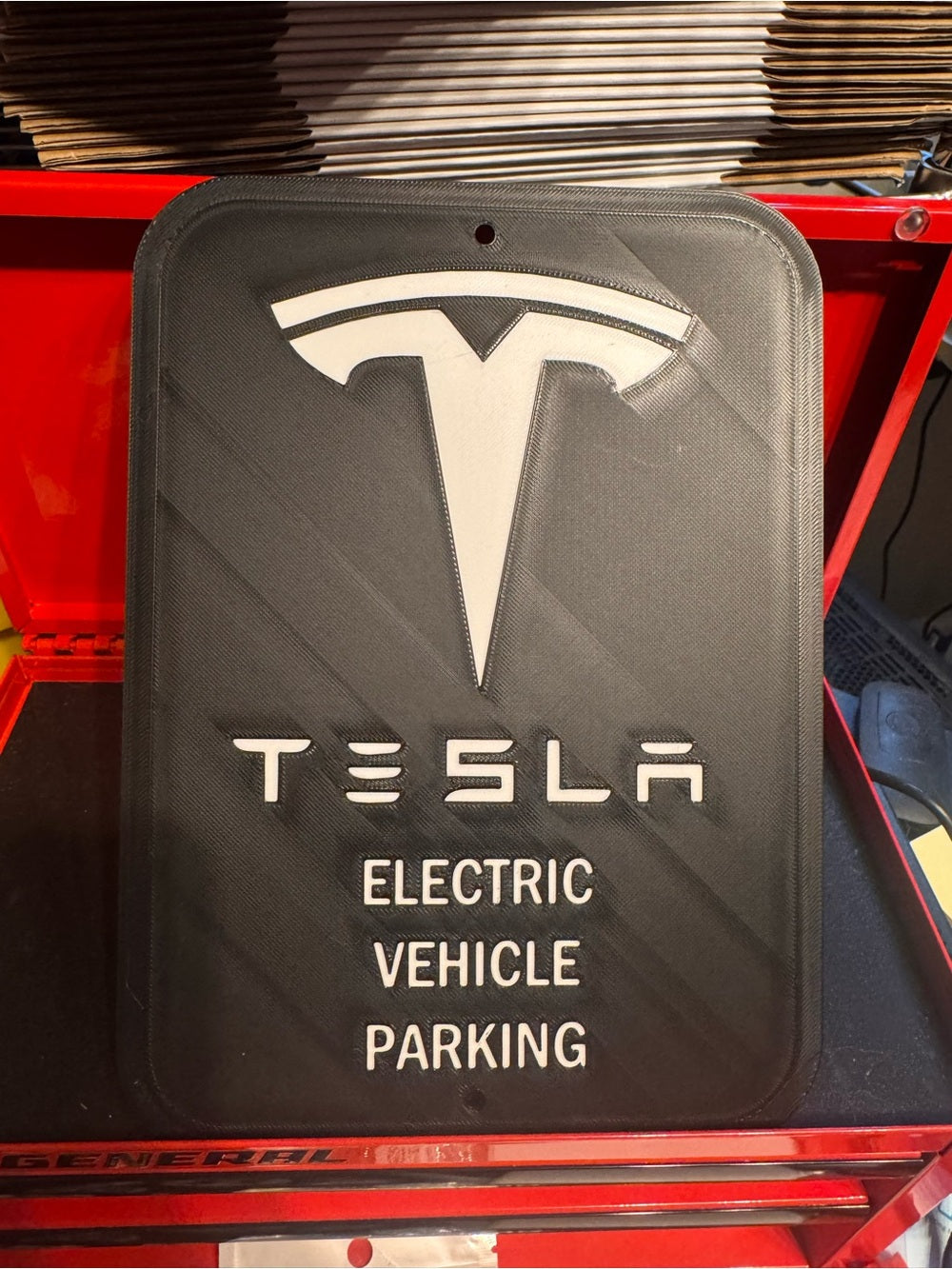 White letters, logo and outline, black background, Tesla EV parking sign in a red tool chest, close view
