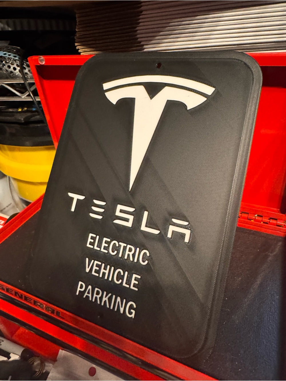 White letters, logo and outline, black background, Tesla EV parking sign in a red tool chest, side view