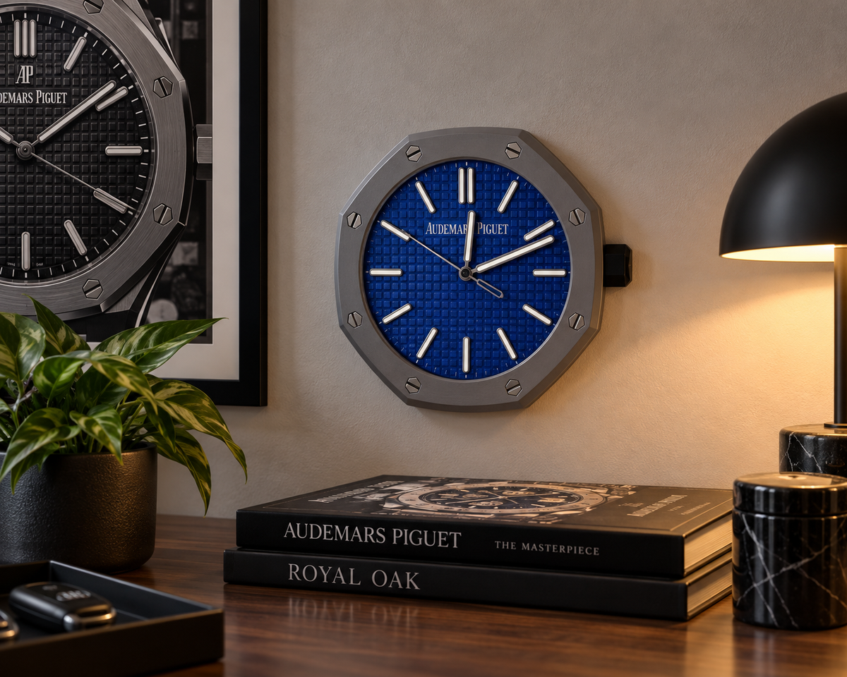 Octagon wall clock with a grey bezel and textured blue dial on a wall above a desk with a lamp and books