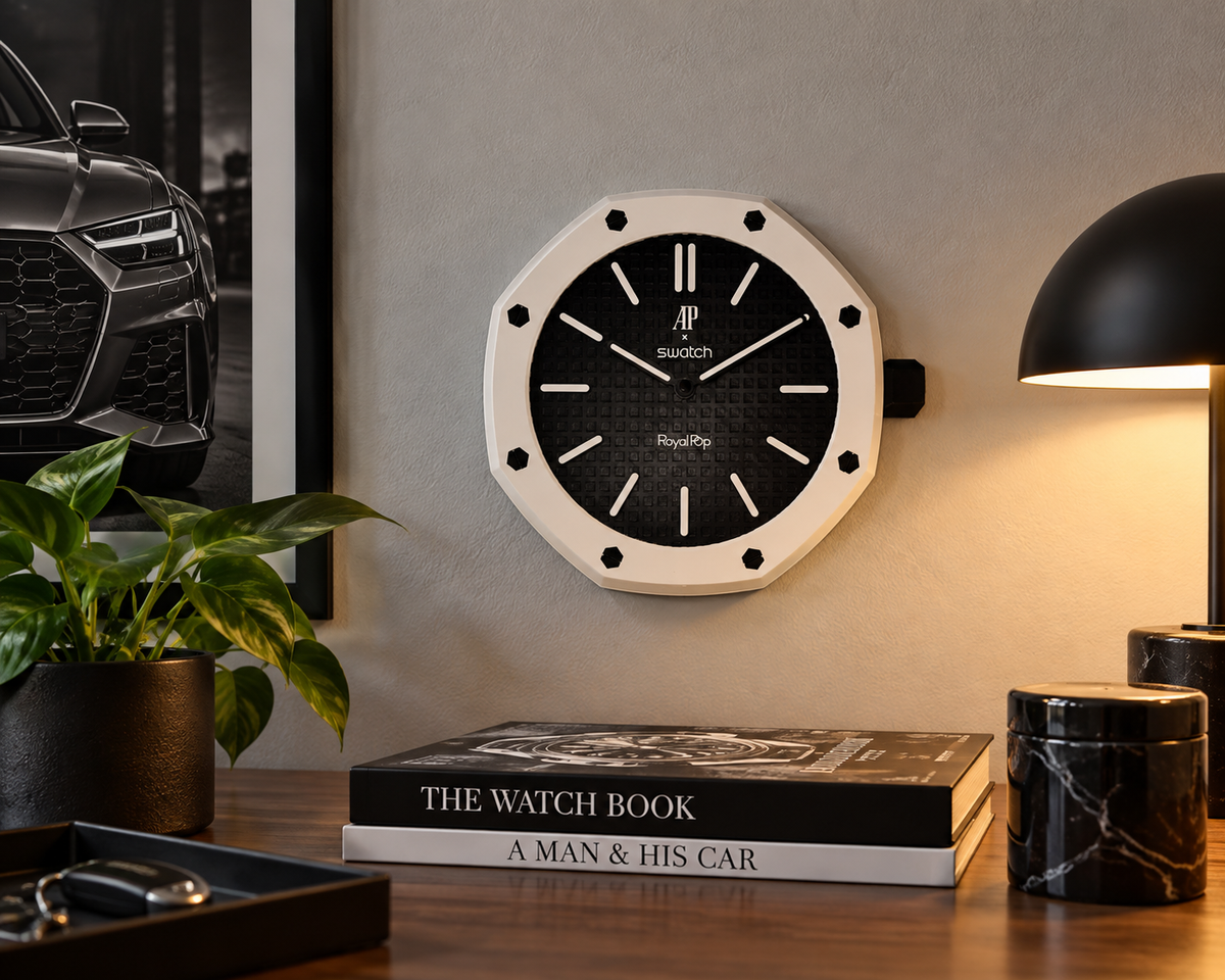 Octagon wall clock with a white bezel and black textured dial on a wall above a desk with a lamp and books