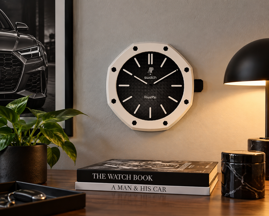 Octagon wall clock with a white bezel and black textured dial on a wall above a desk with a lamp and books
