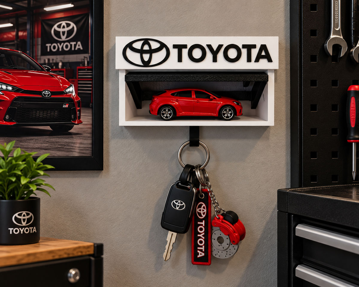 White and black Toyota key holder on a garage wall with a red die-cast Toyota on the shelf and keys on the hook